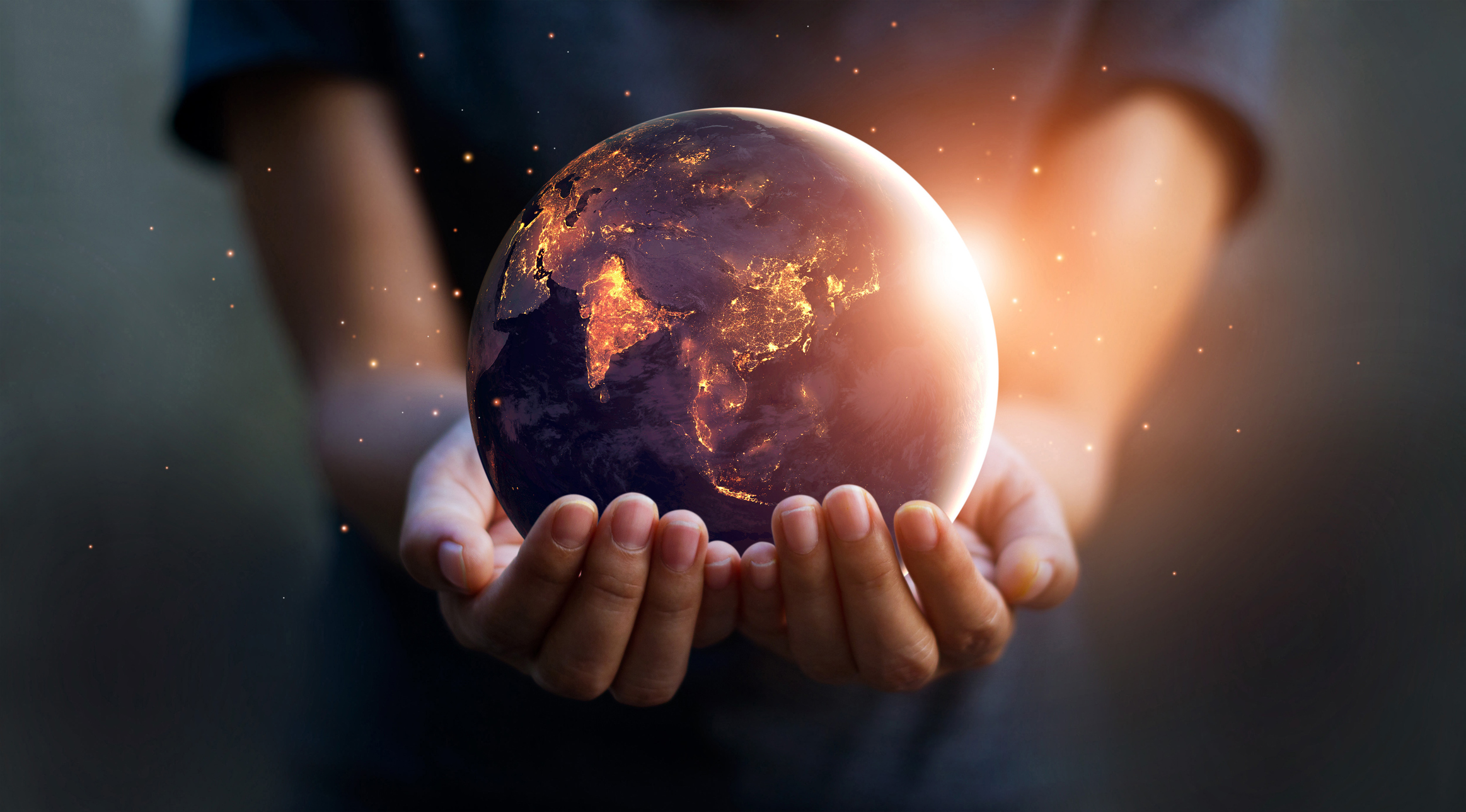 Human hands holding a glowing Earth at night against a dark background, symbolising global impact, trust, and customer testimonials.
